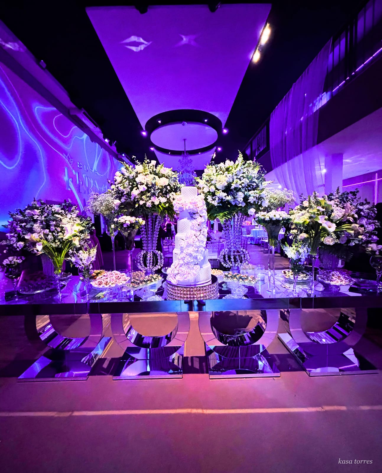 Mesa de bolo de casamento moderna com base espelhada, candelabros de cristal e iluminação cênica violeta — Kasa Torres