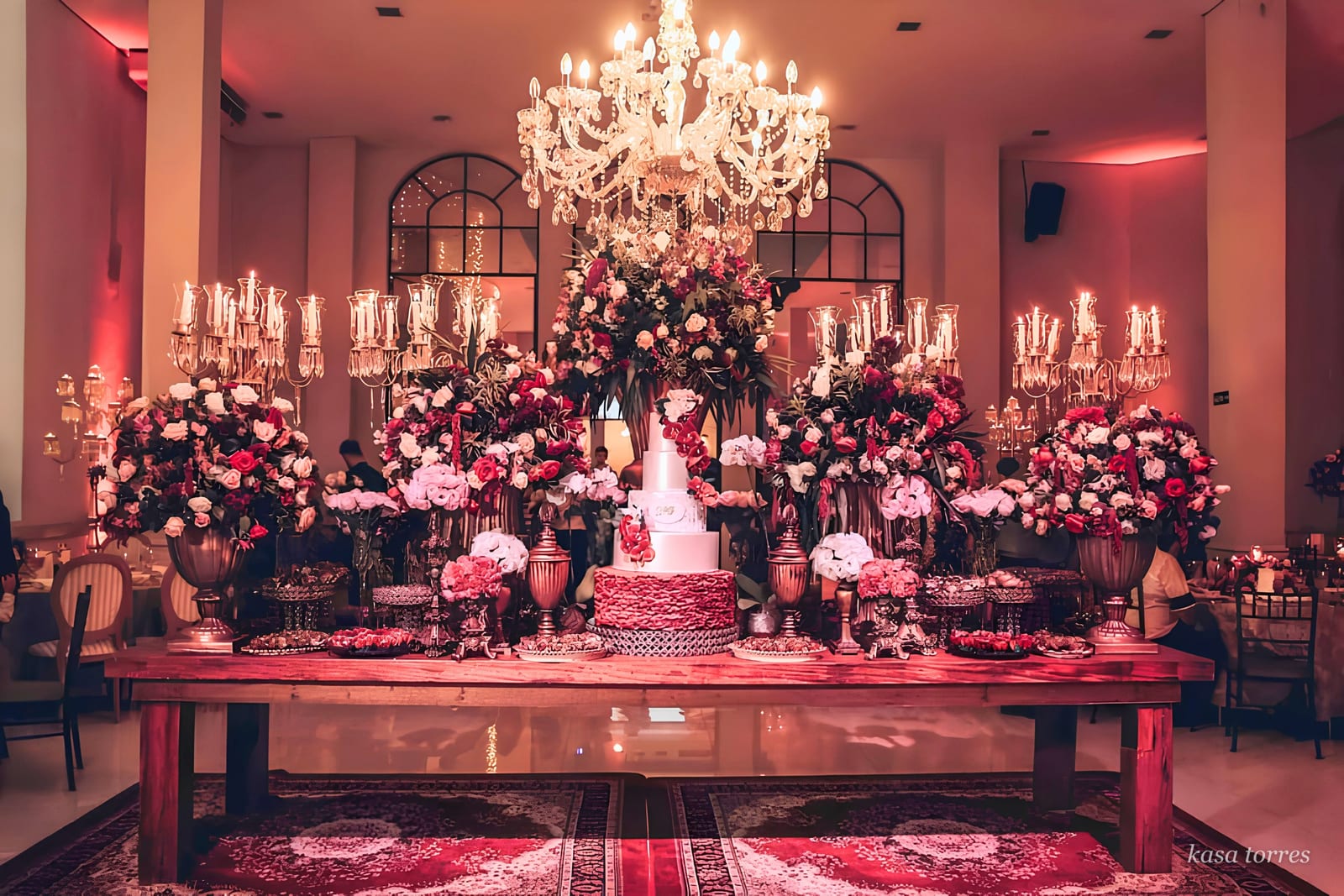 Mesa do bolo de festa de 15 anos com candelabros de cristal e arranjos altos em rosas pink e champagne — Kasa Torres